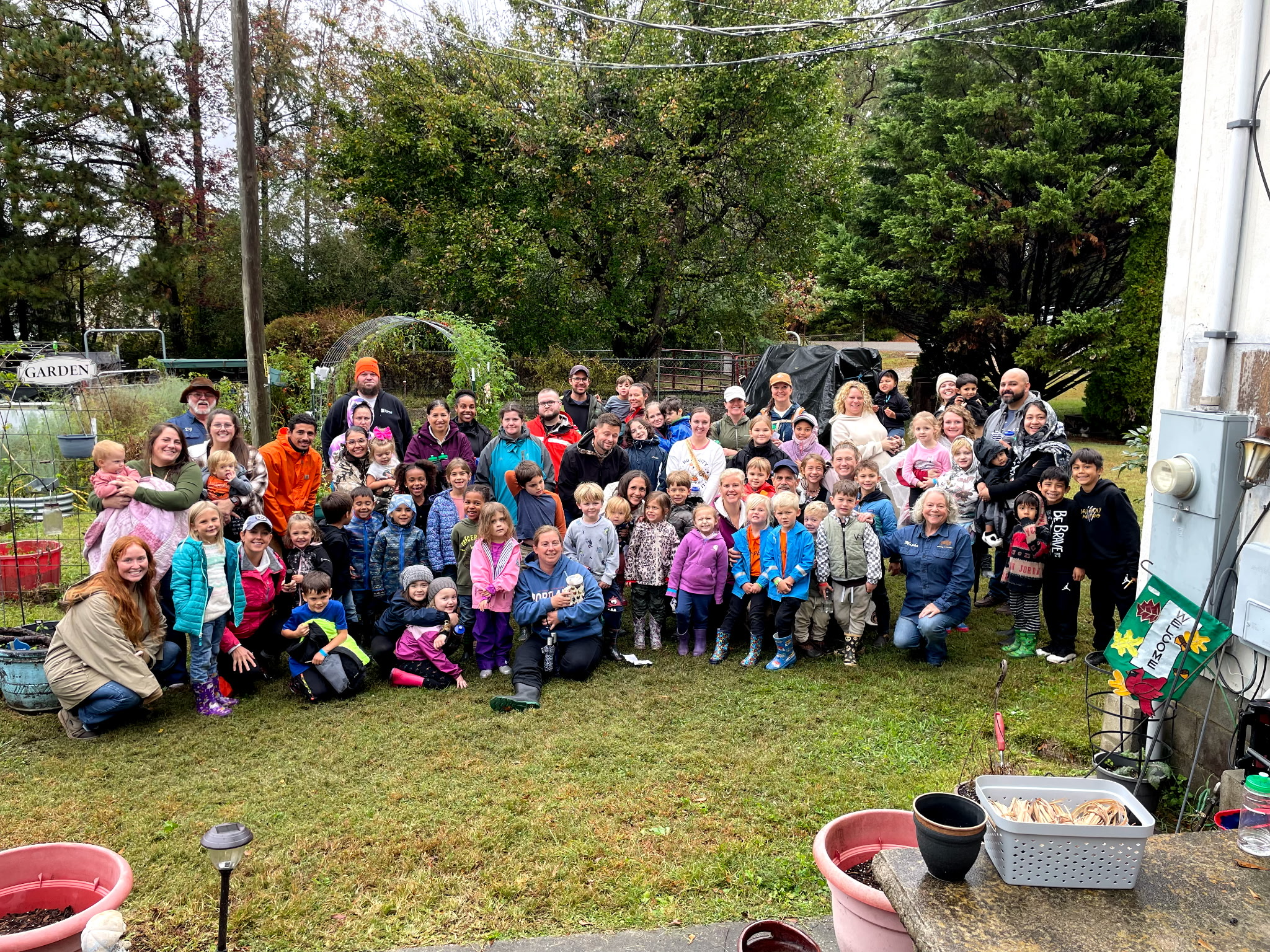 A large group of children and adults gathered in the garden behind the ranch on a fall tour day